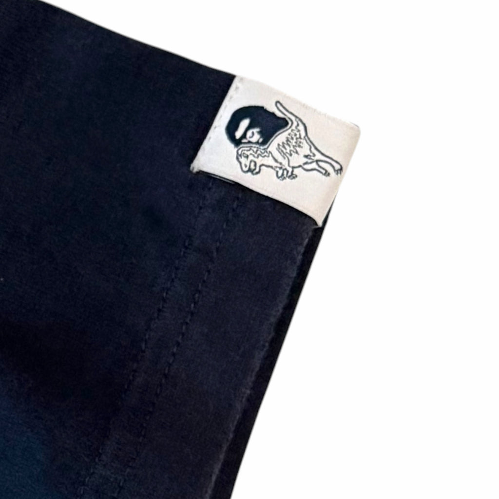 Vangsworld, Inc navy blue cotton t-shirt sleeve featuring a white collaborative BAPE x Coach dinosaur logo tab