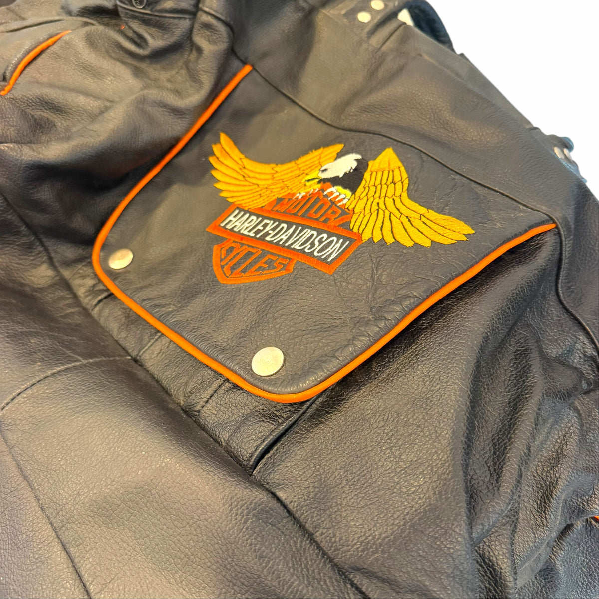 Vangsworld, Inc Harley-Davidson black leather duffel bag with orange piping and eagle logo patch on front pocket